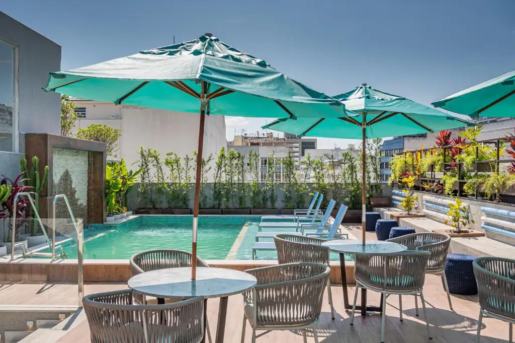 two tables and chairs with umbrellas next to a swimming pool at Royal Regency Palace Hotel in Rio de Janeiro