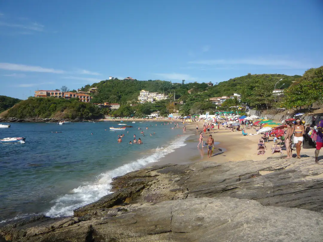 Clear water, beachgoers and green hills at João Fernandes Beach in Búzios