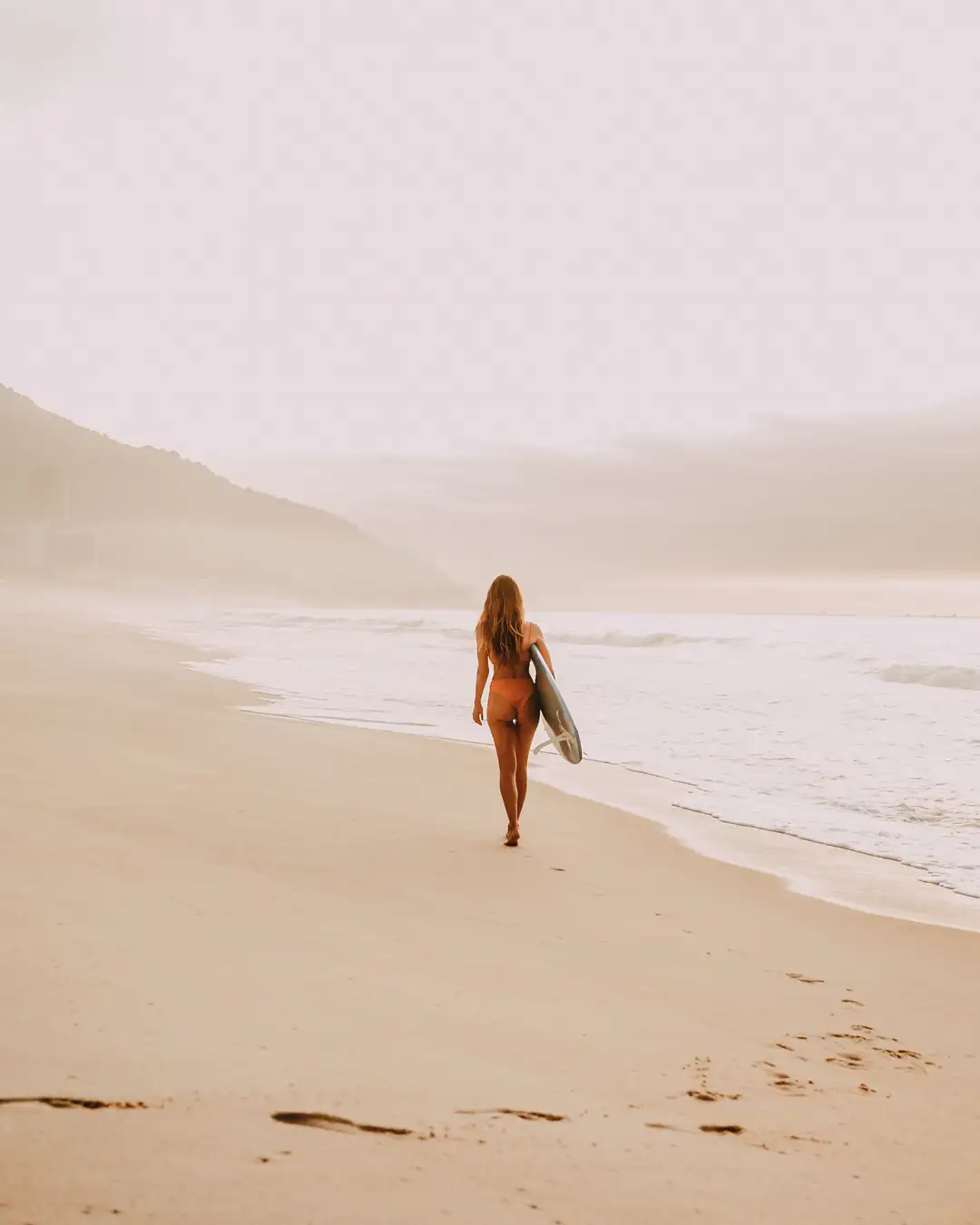 A woman walking independently along the coast with a surfboard