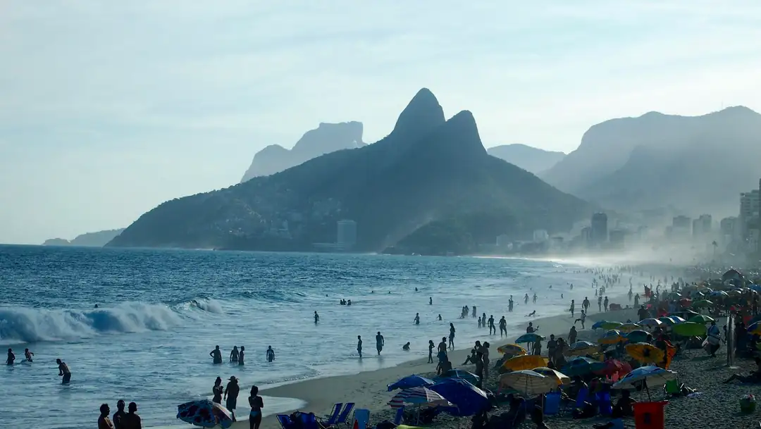 Ipanema beach with umbrellas, ocean waves and mountains beyond